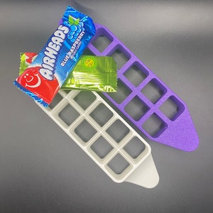 May include: Two purple and white plastic candy organizers with 12 compartments each. The organizers are shaped like a pointed oval. A blue and white Airheads candy wrapper is partially visible in the top compartment of the white organizer.