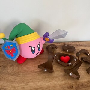 May include: A pink and green character holding a sword and shield. The character is standing on a wooden surface. There are several brown pieces of a puzzle scattered around the character. One piece of the puzzle has a red heart inside.