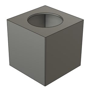 May include: A gray, cube-shaped object with a circular hole in the top. The object has a simple, geometric design and appears to be made of a solid material. The cube is a neutral gray color.