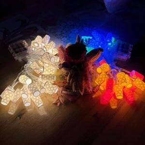 Könnte beinhalten: Eine Lichterkette mit weißen Lichtern mit Punkten, eine Lichterkette mit orangen Lichtern mit Punkten und eine Lichterkette mit blauen Lichtern mit Punkten. Die Lichter sind aneinandergereiht und leuchten.