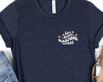 May include: A navy blue t-shirt with the text "Eat Sleep Mahjong Repeat" in white with yellow flower accents.