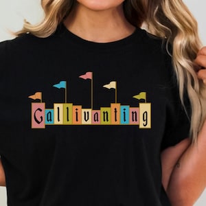 May include: Black t-shirt with a graphic of colorful flags and the word "Gallivanting" in a vintage font.