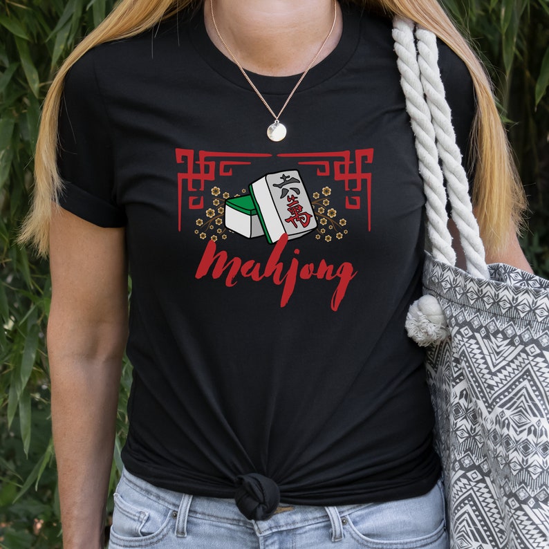 May include: Black t-shirt with a graphic of mahjong tiles and the word "mahjong" in red. The graphic is surrounded by a decorative border and small flowers.