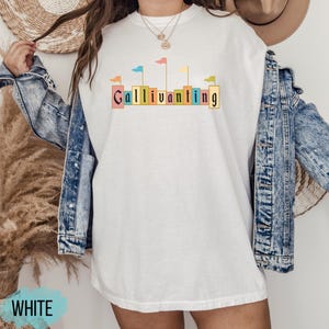 May include: White t-shirt with a graphic of colorful flags and the text "Gallivanting" printed on the front.