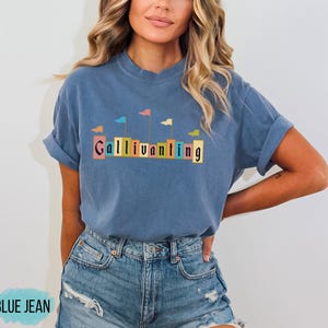 May include: A blue t-shirt with a graphic of colorful flags and the word "Gallivanting" in a vintage font.