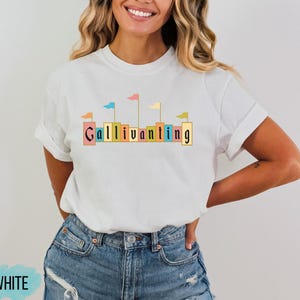 May include: White t-shirt with a graphic of colorful flags and the word "Gallivanting" in a blocky font.