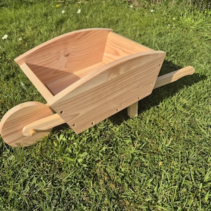 May include: A wooden wheelbarrow with a natural wood finish. The wheelbarrow is empty and has a single wheel.
