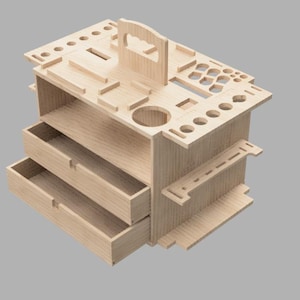 Puede incluir: Un organizador de madera de color claro con dos cajones y múltiples compartimentos. La superficie superior presenta varios agujeros y ranuras, y tiene un asa para facilitar su transporte. El organizador está diseñado para guardar herramientas o suministros.