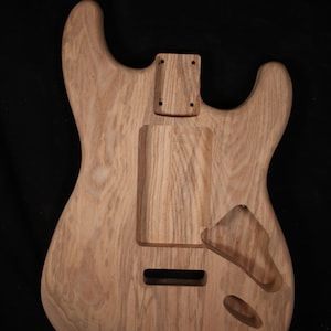 May include: Unfinished wooden guitar body with a natural wood grain finish. The body features cutouts for pickups, a tremolo system, and neck attachment. The guitar body is ready for customization and assembly.