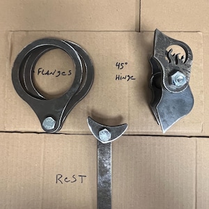 May include: A set of dark gray metal components including two circular flanges, a 45 degree hinge with a flame-shaped cutout, and a T-shaped rest. Each piece is secured with a silver-colored bolt and nut, with labels written in black marker.
