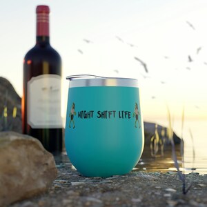 Puede incluir: Un vaso de vino de acero inoxidable turquesa con un gráfico negro de dos figuras caminando y el texto "NIGHT SHIFT LIFE".