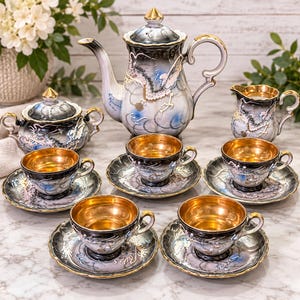 May include: A porcelain tea set featuring a teapot, a lidded sugar bowl, a creamer, and four teacups with matching saucers. Each piece displays a black, white, and blue dragon motif with gold-toned rims and interior cup linings.