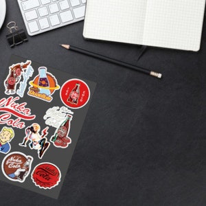 May include: A sheet of stickers featuring various designs from the Fallout video game series. The stickers feature the Nuka-Cola logo, a bottle of Nuka-Cola, and other characters and objects from the game.