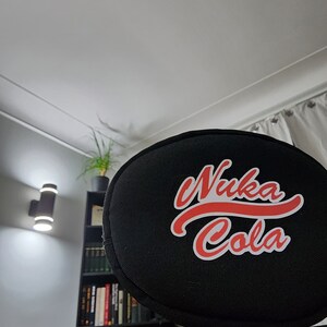 May include: Black round cushion with a red and white "Nuka Cola" logo.