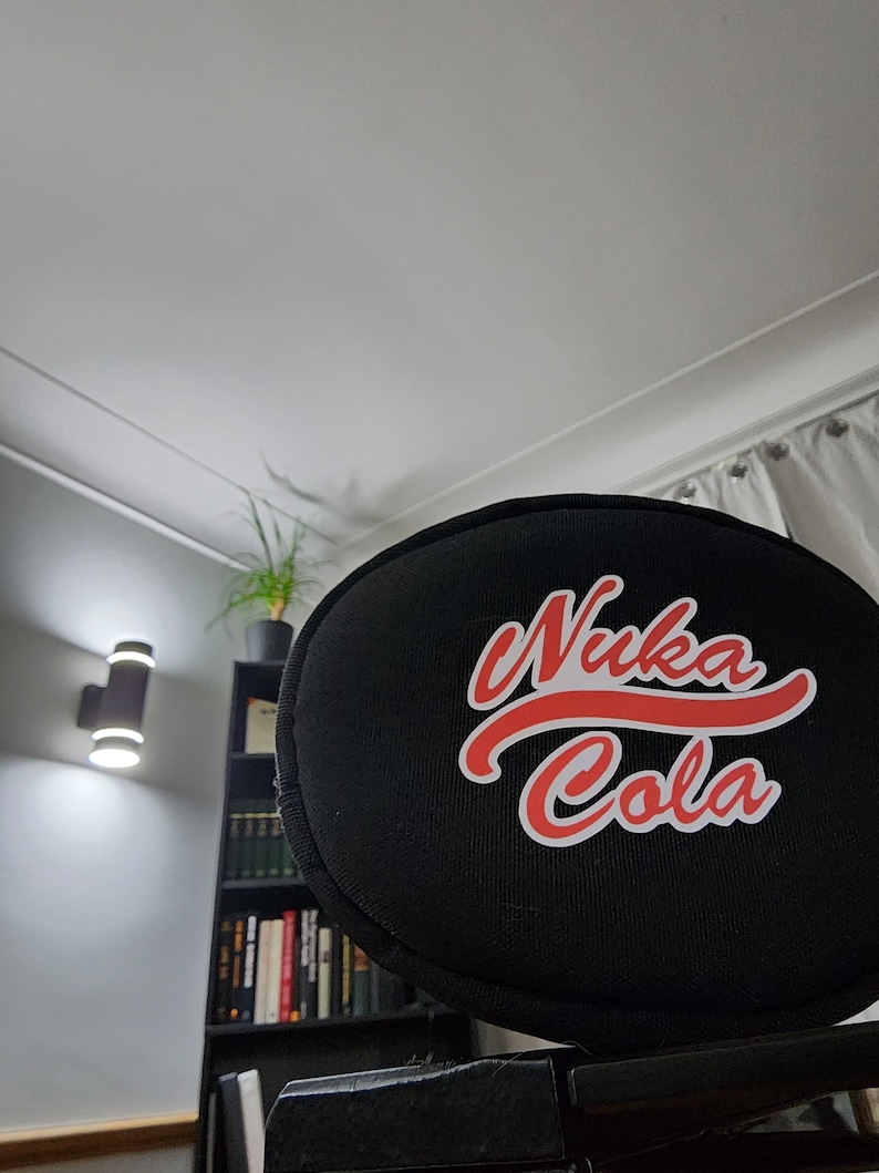 May include: Black round cushion with a red and white "Nuka Cola" logo.