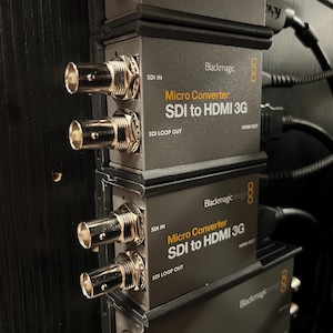 Puede incluir: Una pila de unidades grises Blackmagic Design Micro Converter SDI to HDMI 3G montadas verticalmente. Cada dispositivo cuenta con conectores BNC plateados para los puertos SDI IN y SDI LOOP OUT en el lado izquierdo, con etiquetas en texto blanco y naranja.