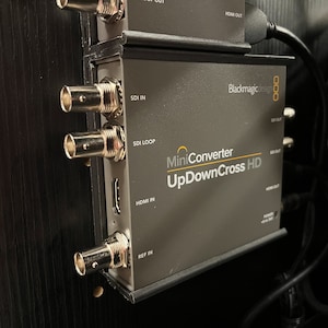 以下が含まれることがあります： 複数のSDIおよびHDMIポートを備えたグレーのBlackmagic Design MiniConverter UpDownCross HDビデオコンバーター。前面パネルには製品名とSDI IN、SDI LOOP、HDMI IN、REF INのラベルが表示されており、側面にはケーブルが接続されています。