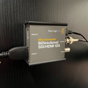 May include: Blackmagicdesign Micro Converter BiDirectional SDI/HDMI 12G converter box with HDMI and SDI inputs and outputs. The box is gray with black trim and white text.