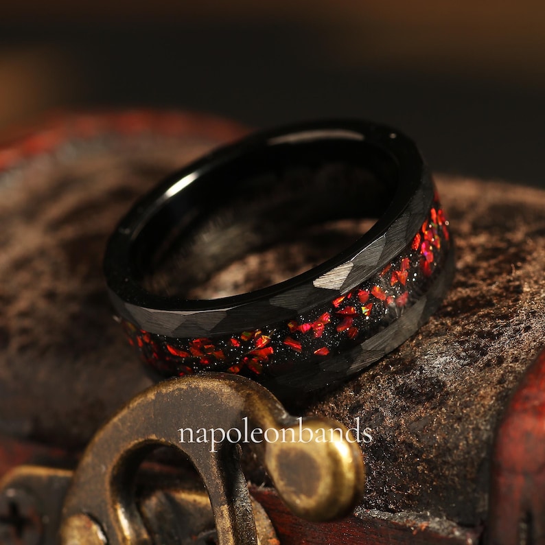 May include: A black tungsten carbide ring with a red and gold glitter inlay. The ring has a faceted, hammered finish.