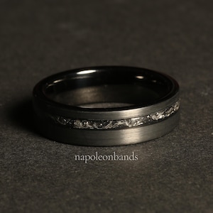 May include: A black tungsten carbide ring with a brushed finish and a silver-colored engraved design.