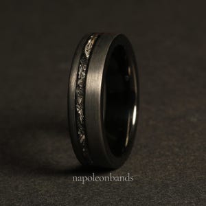 May include: A black tungsten carbide ring with a silver inlay. The ring has a brushed finish and a beveled edge.