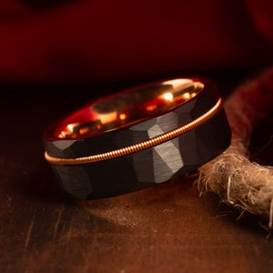 May include: A black and rose gold tungsten carbide ring with a hammered finish and a thin rose gold band around the centre.