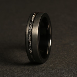 May include: A black tungsten carbide ring with a silver inlay. The ring has a brushed finish and a beveled edge.
