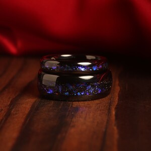 May include: Two black rings with a blue and purple glitter inlay. The rings are stacked on top of each other.