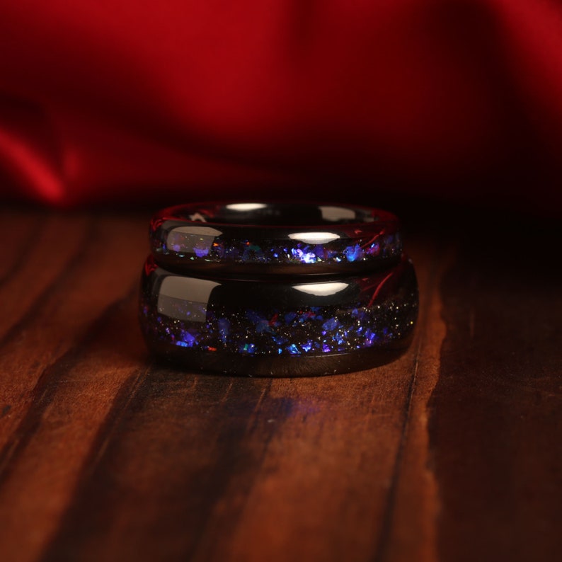 May include: Two black rings with a blue and purple glitter inlay. The rings are stacked on top of each other.
