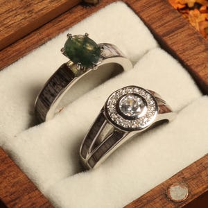 May include: Two silver rings with a green gemstone and a clear diamond in a wooden ring box.