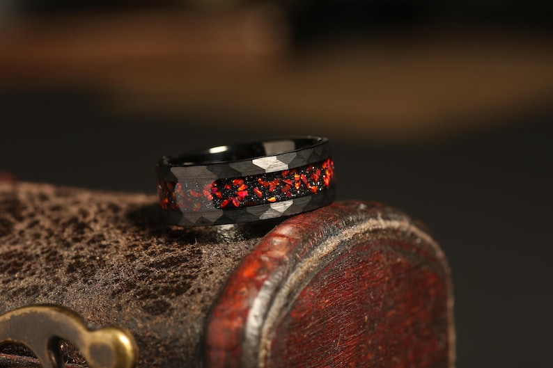 May include: A black ring with a band of red gemstones. The ring is made of a durable material and has a unique design.