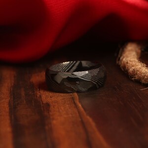 May include: A black ring with a patterned design. The ring is made of metal and has a smooth, polished finish.