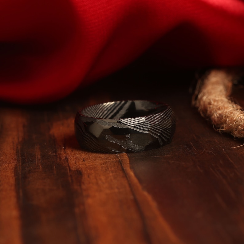 May include: A black ring with a patterned design. The ring is made of metal and has a smooth, polished finish.