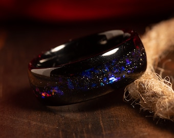 May include: A black ring with a galaxy-like design featuring blue, purple, and gold glitter embedded in the resin.