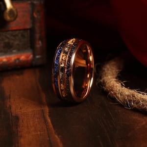 Puede incluir: Un anillo de carburo de tungsteno de oro rosa con una incrustaci&oacute;n azul y dorada. El anillo tiene un acabado pulido y est&aacute; dise&ntilde;ado para hombres.