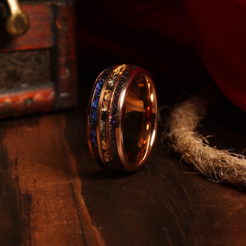 Puede incluir: Un anillo de carburo de tungsteno de oro rosa con una incrustaci&oacute;n azul y dorada. El anillo tiene un acabado pulido y est&aacute; dise&ntilde;ado para hombres.