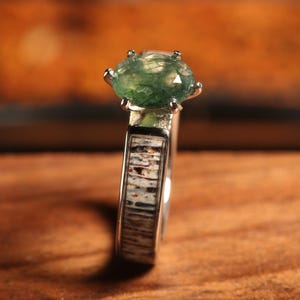 May include: A silver ring with a green gemstone set in a prong setting. The band of the ring is made of antler.