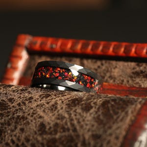 May include: A black tungsten carbide ring with a red and gold glitter inlay. The ring is in a wooden box.