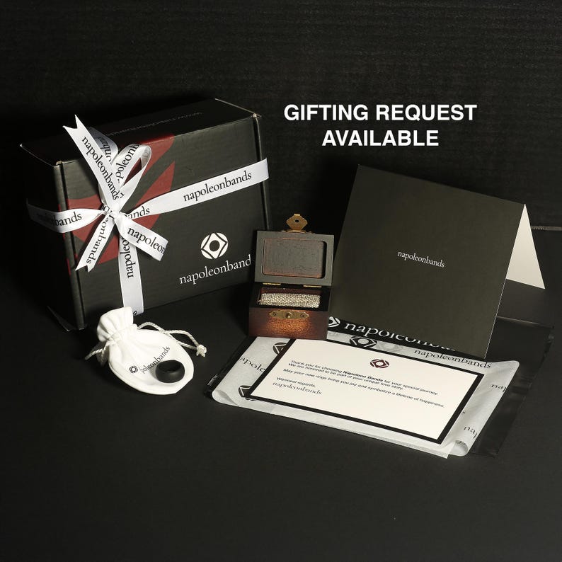 May include: A black gift box with a white ribbon and the text "napoleonbands". A small wooden box with a ring inside is open. A white pouch and a card are also visible. The text "GIFTING REQUEST AVAILABLE" is at the top.