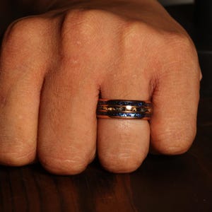 Puede incluir: Un anillo con una incrustaci&oacute;n de madera azul y marr&oacute;n. El anillo est&aacute; hecho de metal y tiene un acabado pulido.
