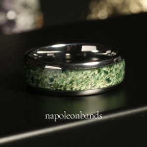 Pode incluir: Um anel de carboneto de tungst&ecirc;nio prateado com uma incrusta&ccedil;&atilde;o de pedra verde. O anel tem um acabamento polido e uma borda chanfrada.