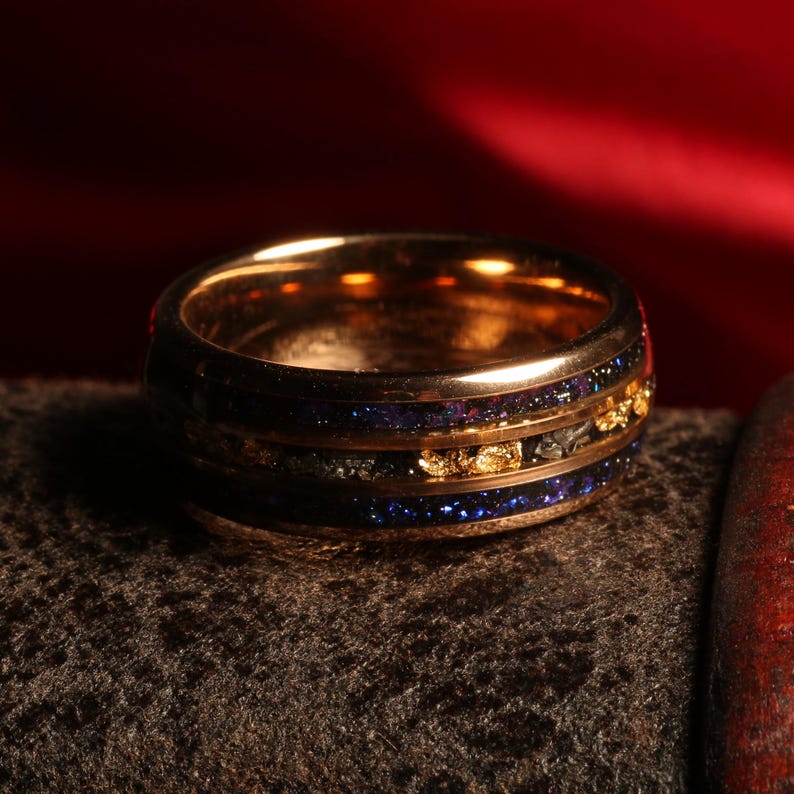 Puede incluir: Un anillo de oro con una incrustaci&oacute;n azul y negra. La incrustaci&oacute;n tiene un patr&oacute;n moteado y motas doradas.