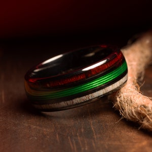 May include: A black ring with green, red, and white inlay. The ring is made of wood and metal.