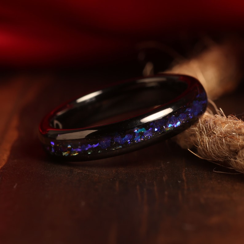 May include: A black ring with a band of iridescent blue glitter embedded in the surface.