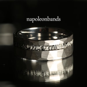May include: A close-up of a silver ring with a textured, faceted band. The ring features a band of small, irregular stones set between the faceted surfaces. The text "napoleonbands" is displayed above the ring.