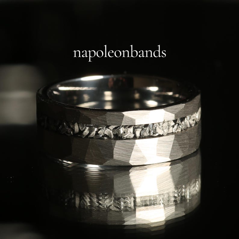May include: A close-up of a silver ring with a textured, faceted band. The ring features a band of small, irregular stones set between the faceted surfaces. The text "napoleonbands" is displayed above the ring.