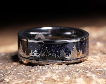 May include: A silver ring with a dark blue, starry inlay depicting a forest silhouette. The ring has a polished finish and a band approximately 8mm wide. The text "napoleonbands" is visible on the ring.