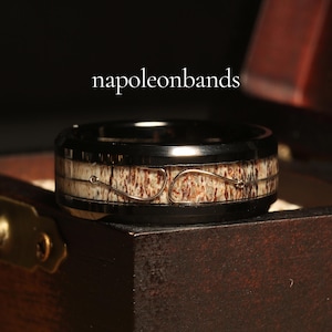 May include: A black tungsten carbide ring with a brown and white antler inlay and a thin silver wire design. The ring is in a wooden box.