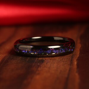 May include: A black ring with a thin band of iridescent blue and purple glitter embedded in the surface.