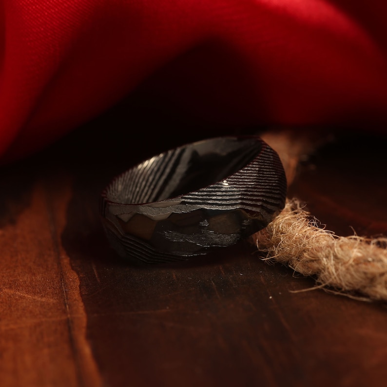 May include: A black ring with a textured, patterned surface. The ring is made of metal and has a polished finish.